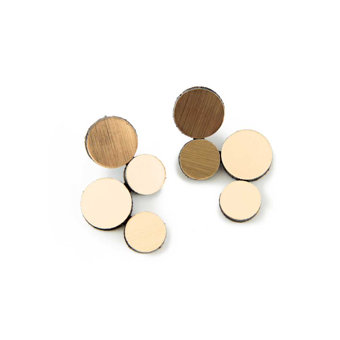Seven round discs in varying sizes and wood shades, inspired by geometric designs, are arranged on a white background. This set is the Abstraction Gold Earrings by Iskin Sisters, featuring both light and dark wood tones.