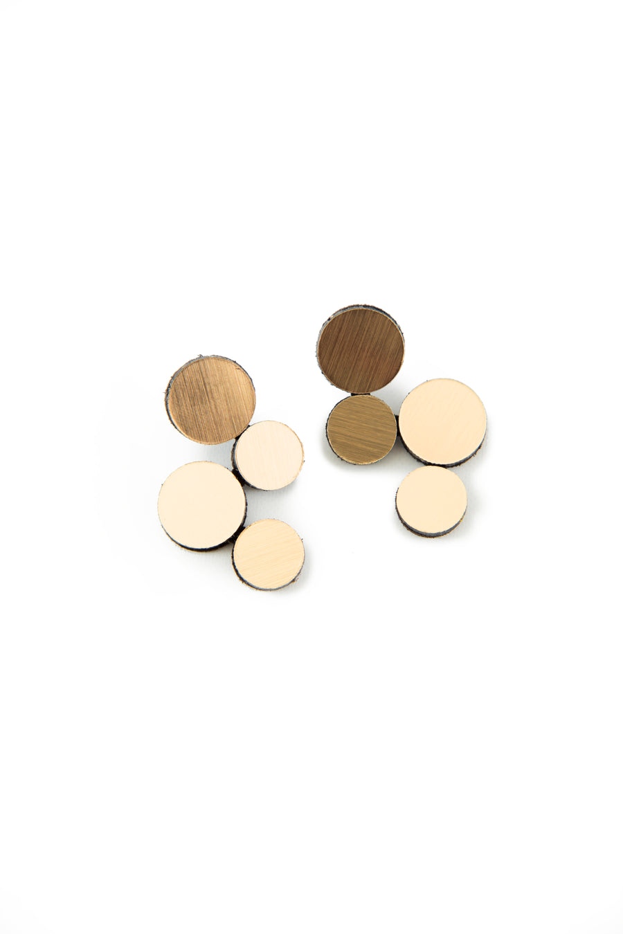 Introducing the Abstraction Gold Earrings from Iskin Sisters: These geometric earrings feature circular discs in a range of brown and beige hues, meticulously arranged in descending order of size. The lightweight discs showcase a wooden texture and are clustered thoughtfully on a white background, radiating subtle elegance.