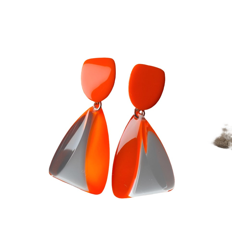 Introducing a pair of bold and contemporary MX.design Acrylic Fluorescent Orange & Clear Earrings. These earrings feature a glossy rectangular top connecting to a trapezoidal drop, combining vibrant orange and sleek clear elements in an asymmetrical, modern design.