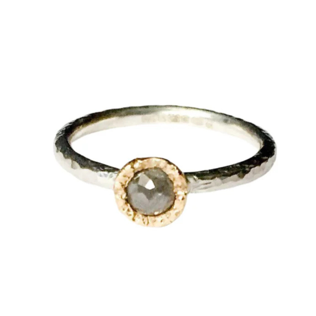 A minimalist ring featuring a single, round grey diamond set in a textured gold bezel on a slim, hammered finish sterling silver stacking ring. The Aurous Ring Silver Grey Diamond by Abbie Dixon is placed against a plain white background.