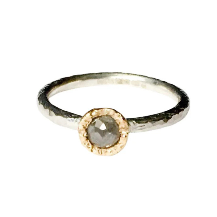 A minimalist ring featuring a single, round grey diamond set in a textured gold bezel on a slim, hammered finish sterling silver stacking ring. The Aurous Ring Silver Grey Diamond by Abbie Dixon is placed against a plain white background.