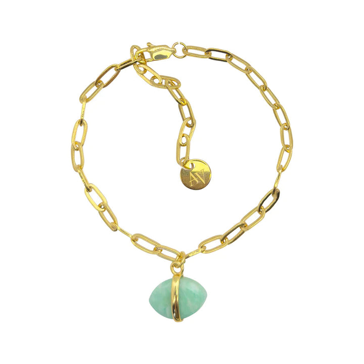 The Ayin Bracelet by Aria V is a gold electroplated chain bracelet with a paperclip-style design, an adjustable clasp, and a round gold tag engraved with the letters "A V." This piece of handmade jewelry features a single pendant made of green translucent stone encased in gold.