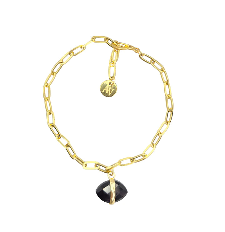 The Ayin Bracelet from Aria V, with its rectangular gold chain links, is a perfect example of handmade jewelry, featuring a small round pendant engraved with "AV" and adorned with a black faceted gemstone charm hanging from the center.