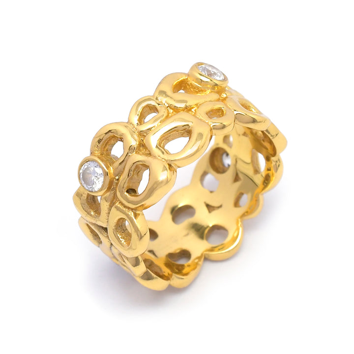 A handmade gold ring with an intricate, openwork design featuring interconnected loops and two small, embedded gemstones is pictured. The Bordeaux Ring by Shyla has a wide band and a shiny, polished surface, highlighting the detailed craftsmanship and the sparkle of the stones. Perfect as hypoallergenic jewellery.