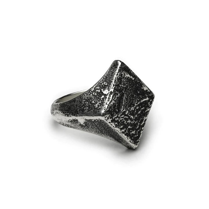 A patinated 925 silver ring with a textured, square-shaped top. Its rugged, hammered finish gives it a rustic and handcrafted appearance. The slightly tapered band and angled square top add to its distinctive style, making it a standout piece of handmade jewelry. Presenting the Diamond Signet Ring by Septentrion.