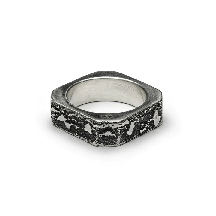 Septentrion's Nut Ring features a hexagonal design with a rustic, textured black and silver band. Crafted from patinated 925 silver, the ring boasts unique patterns and an artisanal design with a rough, weathered appearance, giving it a distinctive and rugged aesthetic. A true piece of handmade jewellery.