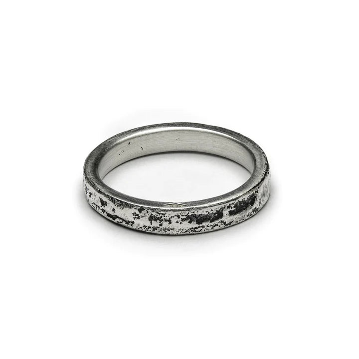 A weathered, silver-colored ring with a textured surface is shown against a plain white background. Crafted from Patinated 925 silver, this piece of handmade jewellery has a rustic, aged appearance, giving it unique variations and a vintage look. This is the Thin Ribbon Ring by Septentrion.