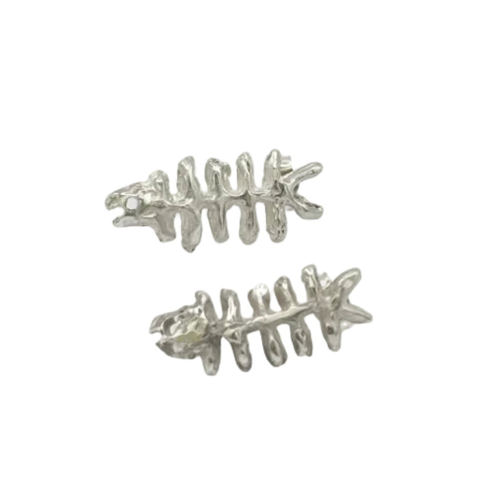Baraka Earrings by Soufana Attia—silver, fishbone-shaped, inspired by Arab symbols of protection and Baraka—are displayed on a plain light gray background with generous empty space.
