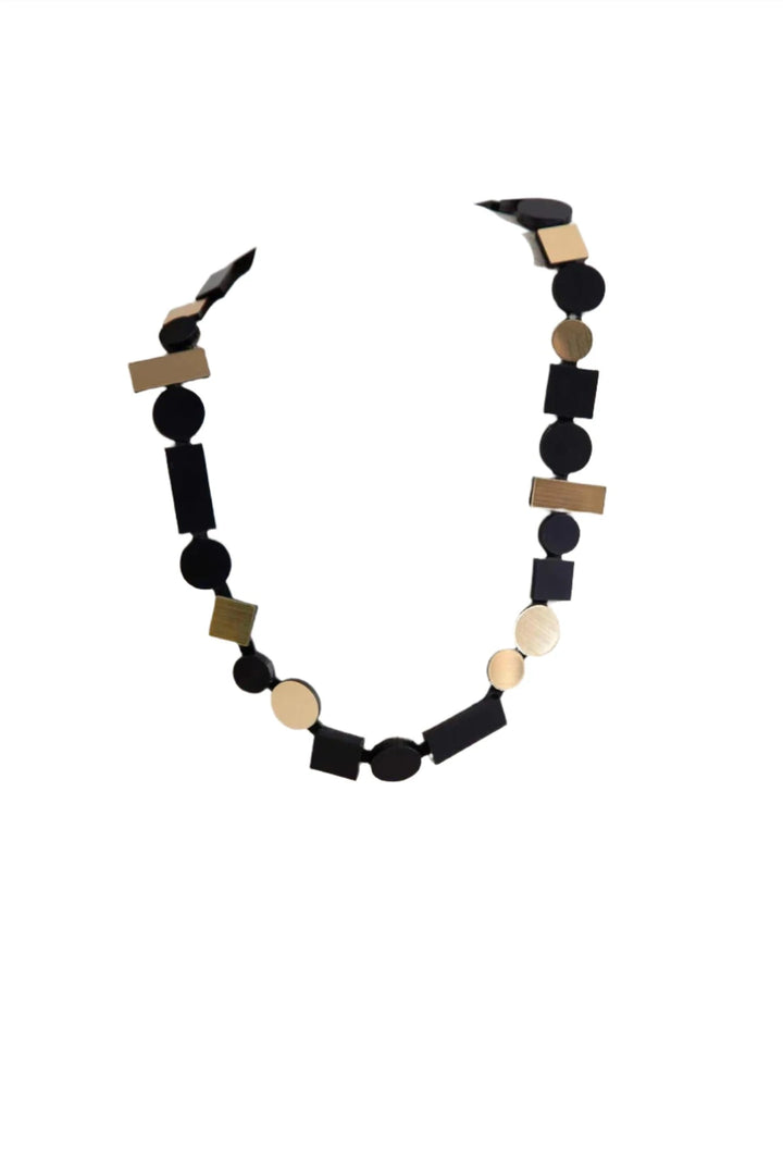 A contemporary necklace from the Bauhaus Collection, known as the Bauhaus Black & Gold Necklace by Iskin Sisters, is displayed on a white textured mannequin bust. This statement piece features a chain of variously sized black and gold geometric shapes, including circles, squares, and rectangles, creating a modern and artistic design.