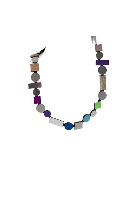 Introducing the Bauhaus Rainbow Necklace by Iskin Sisters: a statement piece that showcases an eclectic mix of geometric beads in various shapes and vibrant colors, including circles, rectangles, and squares. The beads feature predominantly blue, green, purple, gray hues and metallic tones, all arranged in an eye-catching asymmetrical pattern.