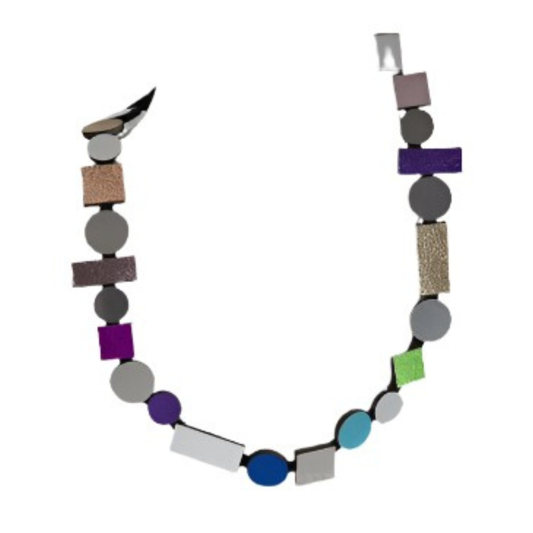 The Bauhaus Rainbow Necklace by Iskin Sisters features bold geometric shapes—circles, squares, and rectangles—in vibrant colors and textures along a curved strand, making it a striking statement piece.