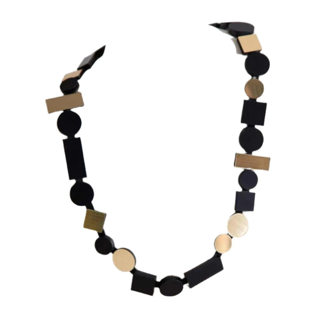 The Iskin Sisters Bauhaus Black & Gold Necklace features alternating rectangular and round shapes with gold-tone accents, arranged in a bold geometric pattern inspired by Bauhaus design.