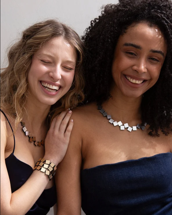 Two smiling women wearing Bauhaus Round Squares Necklace - Silver necklaces and a bracelet made of metallic square tiles.