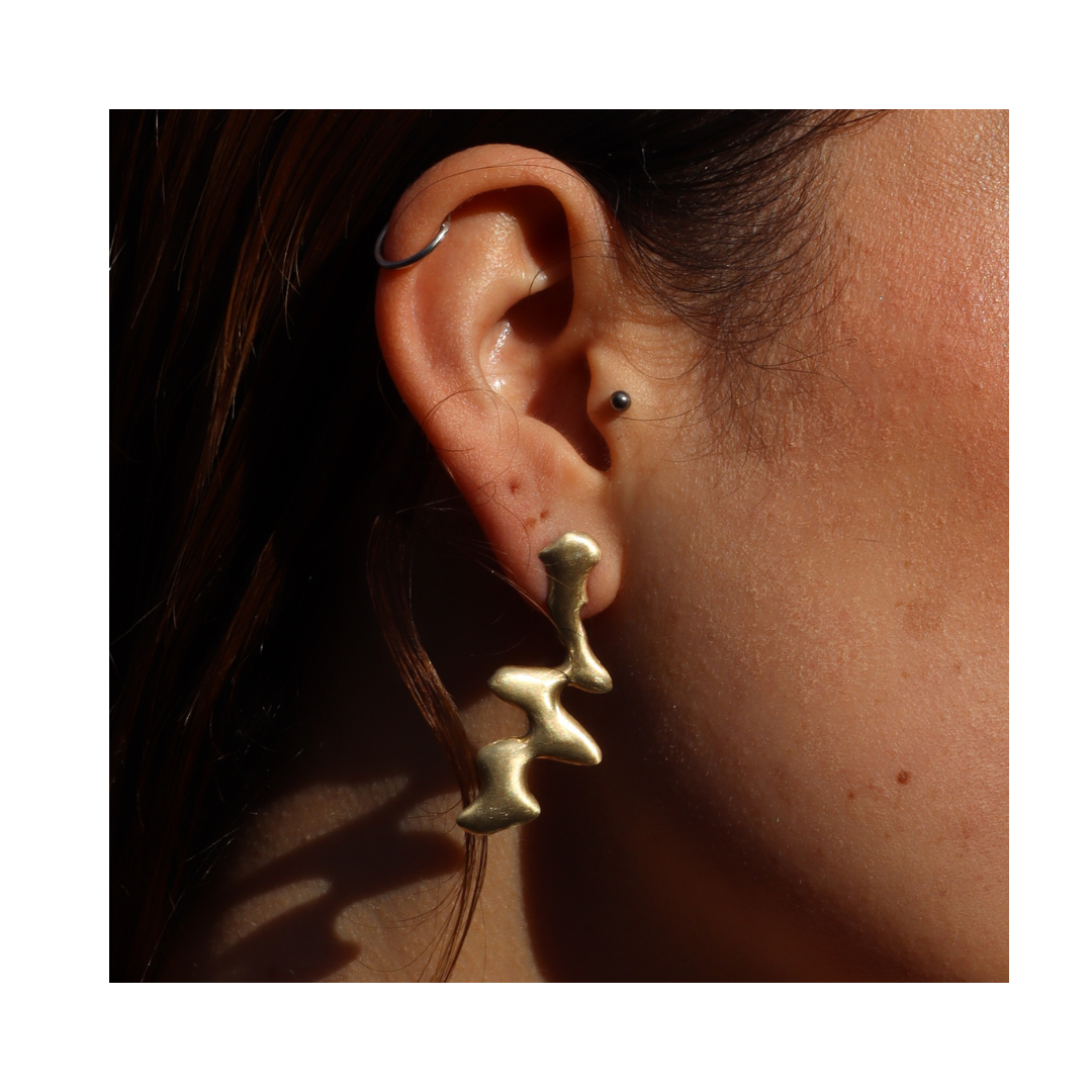 Close-up of an ear wearing the Blaze Studs by Madeleine Sculptural Jewellery, a small nose stud, and a silver hoop. Warm lighting highlights the unique lines—ideal for fans of sculptural earrings and bold style statements.