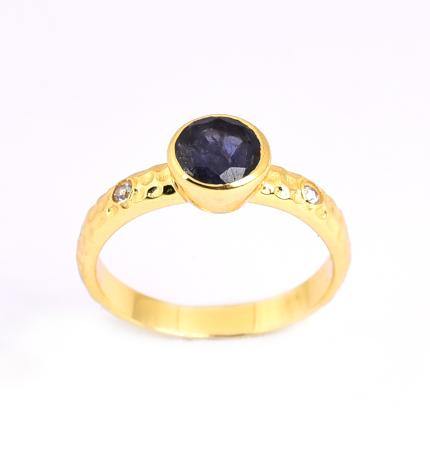 A gold vermeil ring with a dark blue quartz gemstone set in the center. The band features two small clear stones on either side of the main gemstone and a slightly textured surface. The ring is displayed against a plain, light background. The Midnight Sky Ring by Watermelon Tropical.