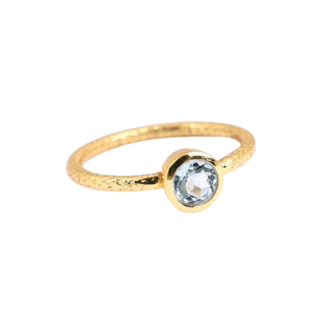 The Blue Topaz Solitaire Gold Ring by Watermelon tropical is a thin gold vermeil band with a hammered texture, featuring a single round blue topaz gemstone in a simple bezel setting.