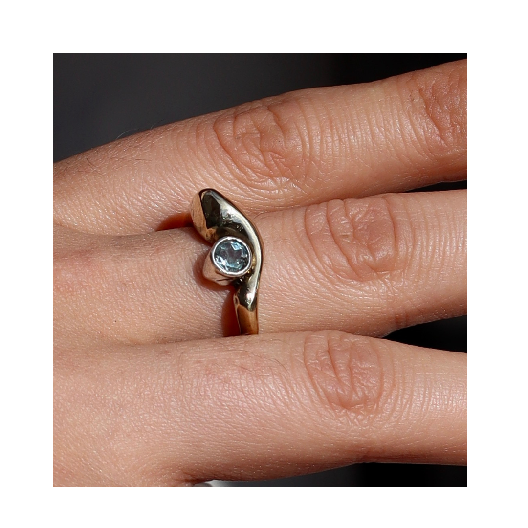 A close-up of a hand wearing the Bough Ring by Madeleine Sculptural Jewellery, featuring an asymmetrical, organic gold design with a central round clear gemstone that highlights artisan craftsmanship.