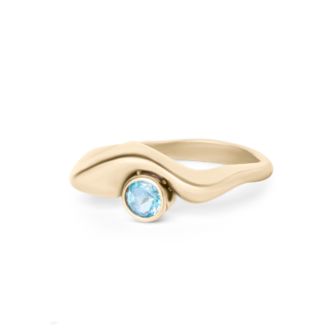 The Bough Ring by Madeleine Sculptural Jewellery features a flowing, organic gold design with a round blue gemstone set asymmetrically, showcasing smooth curves and a modern, artistic style.