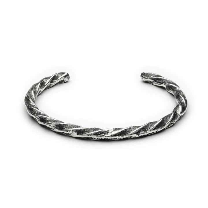 The Septentrion Twisted Bracelet, an open-ended, twisted metal bracelet with a rugged, textured surface, likely made of patinated 925 silver. The bracelet has a slightly rustic and handcrafted appearance, showcasing its artistic design and unique craftsmanship.