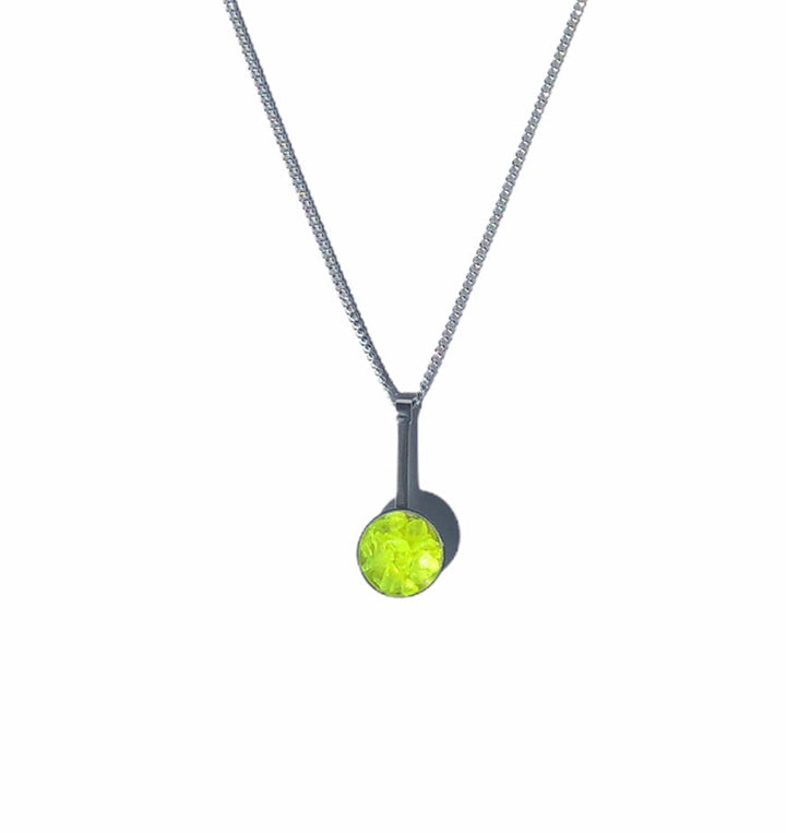 The Angela O'Keefe Neon Dome Drop Pendant in sterling silver features a slim setting with a vibrant fluorescent gem (available in pink or yellow), and it hangs elegantly from a box chain, showcasing its modern and striking hue against a plain white background.