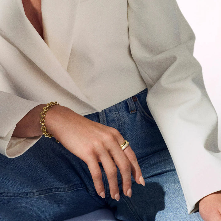 A person in a white blazer and blue jeans, with their hand resting on their knee, showcases the Sif Jacobs Carrara Bracelet Silver—an elegant accent ideal for any demi-fine jewellery collection.