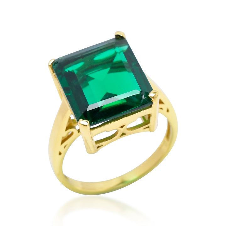 The Claudia Ring by Shyla is a vintage-inspired ring featuring a large, square-cut emerald green stone. Crafted from 22 carat gold, the ring boasts an ornate design with delicate cut-out details on the sides, highlighting the vibrant green hue of the emerald.