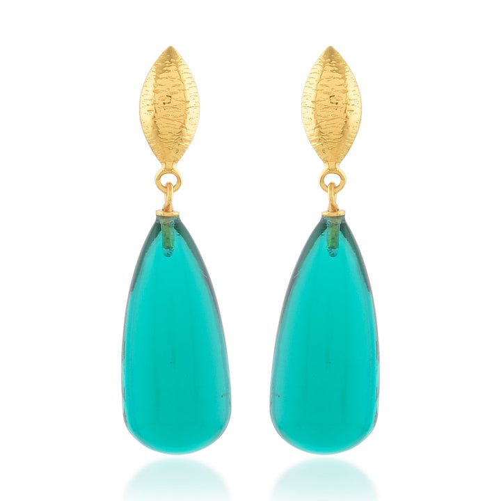 The Corine Earrings by Shyla are a pair of elegant, hypoallergenic drop earrings featuring gold, leaf-shaped studs at the top and elongated, teardrop-shaped turquoise stones dangling below. The smooth and glossy turquoise stones add a vibrant pop of color to this exquisite design.