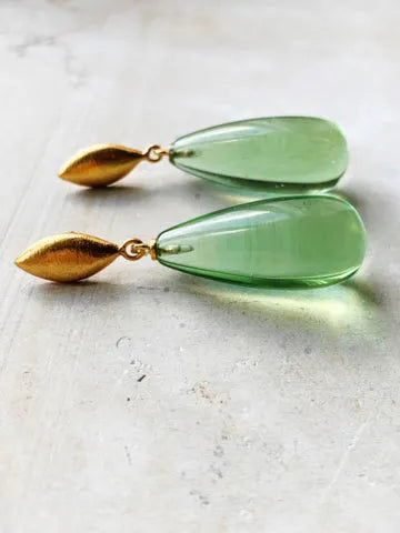 Shyla's Corine Earrings in gold on silver showcase an elegant leaf-shaped stud and a translucent green teardrop-shaped pendant. These hypoallergenic pieces are beautifully presented on a light gray surface.