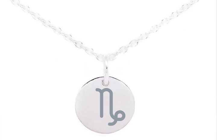 A silver necklace with a round pendant featuring the Capricorn zodiac sign. The Capricorn symbol is etched in gray on the shiny, reflective surface of the pendant. The delicate, lightly twisted chain holds this sterling silver charm beautifully against the plain white background. This is the Horoscope Large Disc Charm Silver by Personalised Charms.