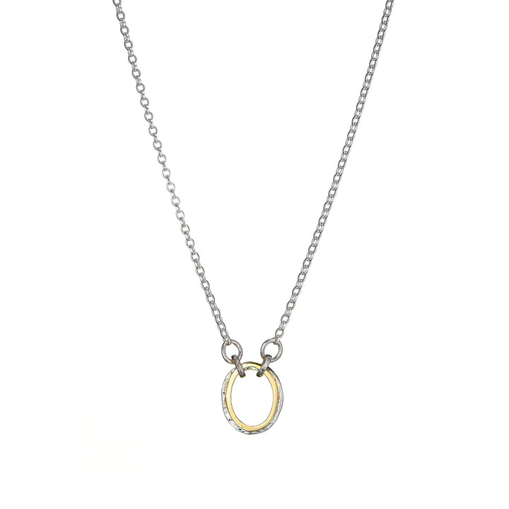 A delicate silver chain necklace with a small, circular pendant at the center. The pendant has a gold-toned inner circle and a silver-toned outer edge, creating a simple yet elegant design. Paired perfectly with matching Carran Mix Pendant earrings by Lynsey de Burca, the set is displayed against a clean white background.