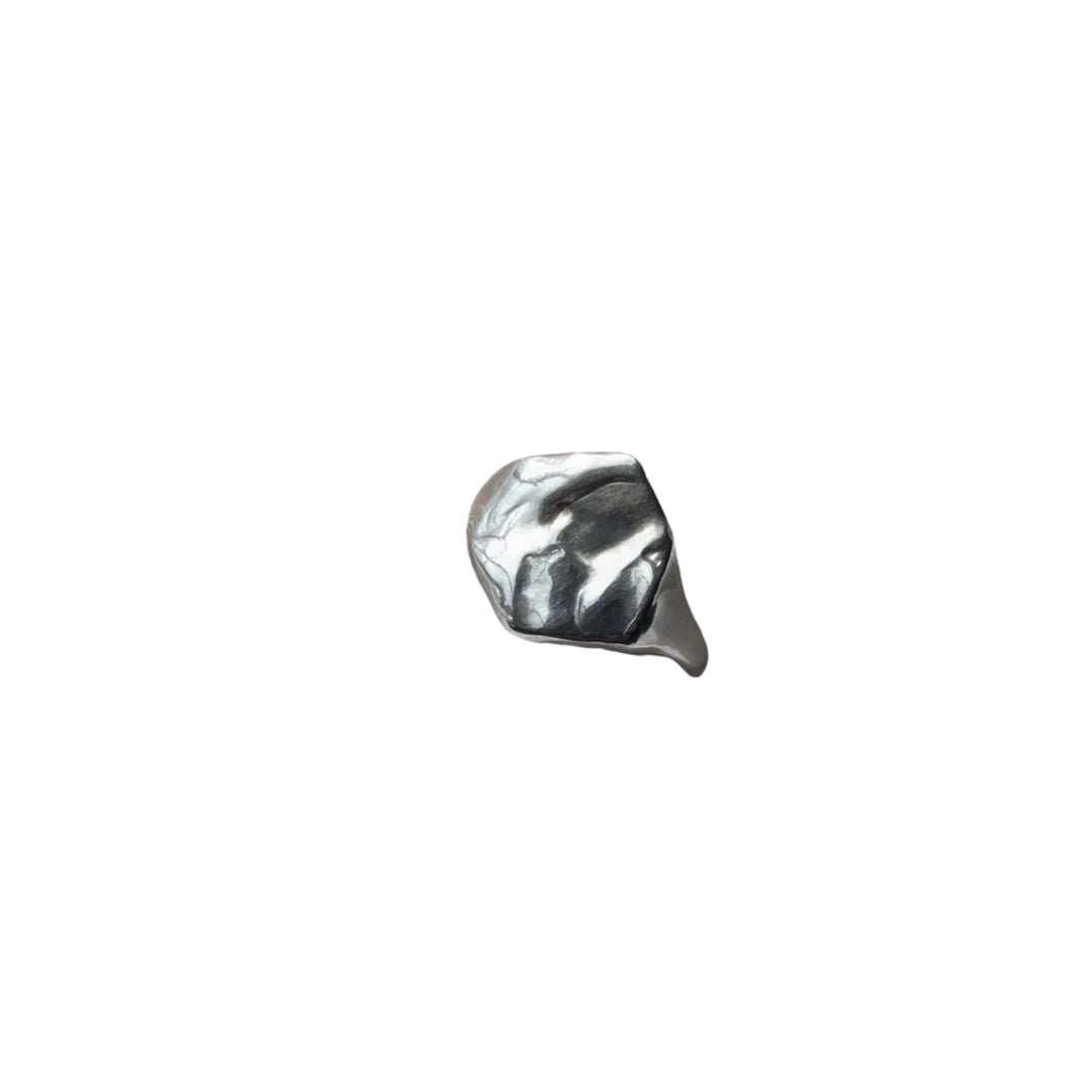 A Causeway Coastal Silver Signet Ring by Becca Calmont, made from shiny recycled sterling silver, sits on textured white fabric with natural light highlighting its unique form.