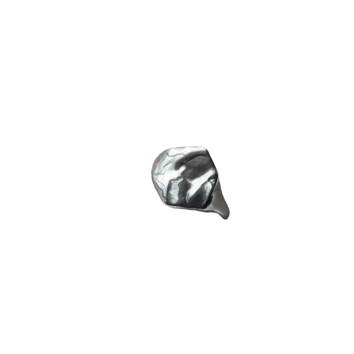A Causeway Coastal Silver Signet Ring by Becca Calmont, made from shiny recycled sterling silver, sits on textured white fabric with natural light highlighting its unique form.