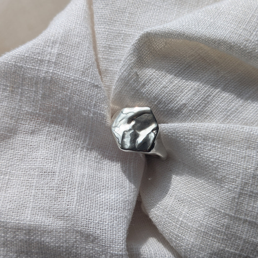 The Causeway Coastal Silver Signet Ring by Becca Calmont, crafted from recycled sterling silver with an organic top inspired by the Giant’s Causeway, rests on textured white fabric in natural light.
