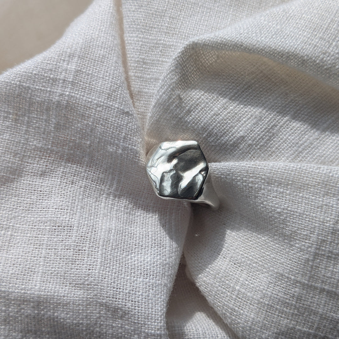 The Causeway Coastal Silver Signet Ring by Becca Calmont, crafted from recycled sterling silver with an organic top inspired by the Giant’s Causeway, rests on textured white fabric in natural light.