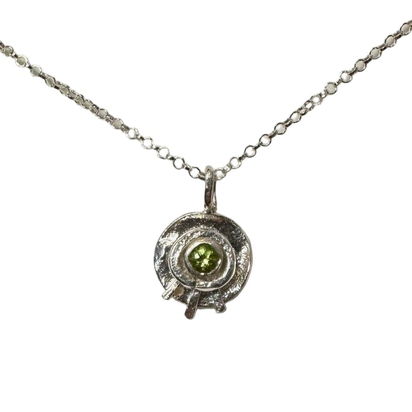 Round shaped silver pendant with peridot stone in the centre. Appears similar to an eye shape.  