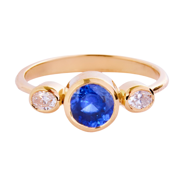 The Celestial Halo 18ct yellow gold ring by Madeleine Fine Jewellery features a central blue sapphire accented by two natural diamonds, offering a stunning and elegant design.