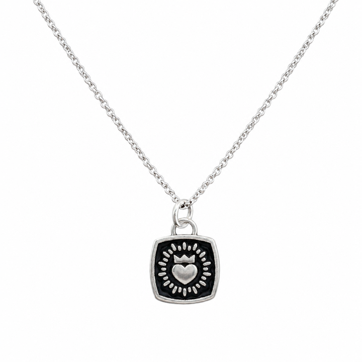 The Collective Dublin’s Double Sided Keith Haring Pendant with Chain is a handmade silver necklace from Dublin, featuring a square-shaped pendant with a raised heart encircled by a sunburst pattern on a black background, inspired by Keith Haring’s iconic designs.