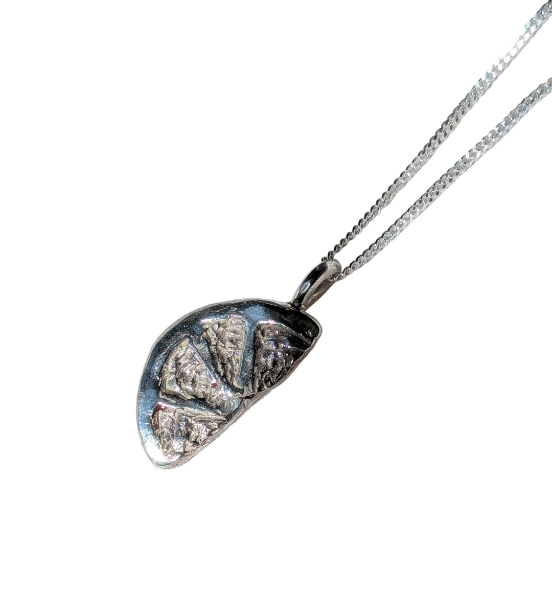 The Becca Calmont Citrus Slice Pendant, a silver necklace with a chunky chain and abstract textured pendant, rests on soft white fabric in bright natural light—perfect as summer jewelry.