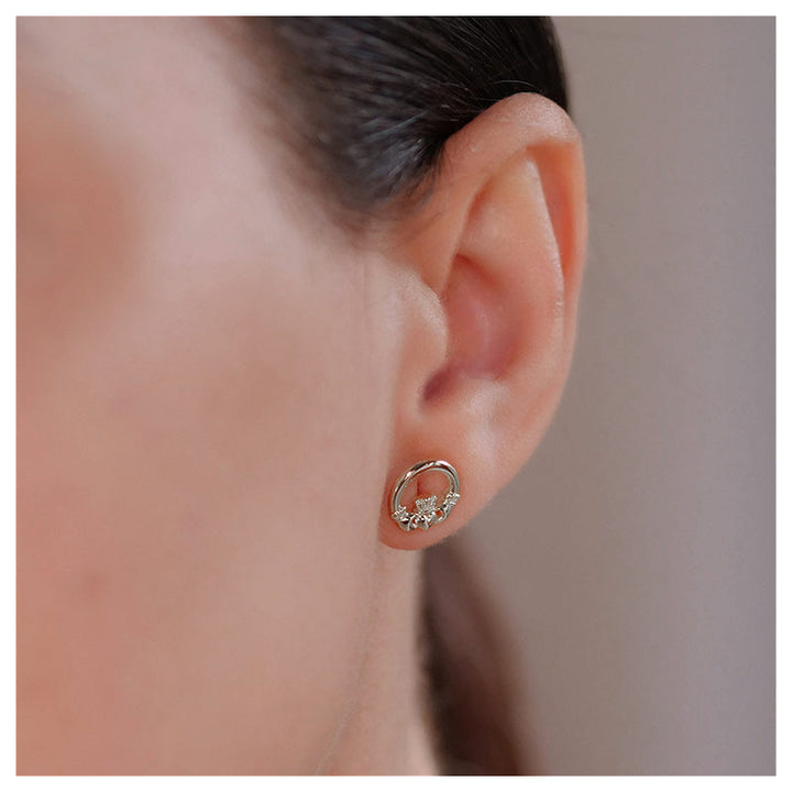 A close-up of a person's ear wearing ShanOre Sterling Silver Claddagh Studs, featuring decorative details, against a neutral background.