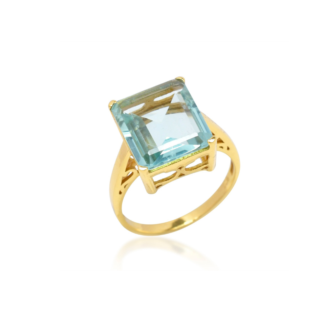 The Claudia Ring by Shyla is a vintage-inspired gold-on-sterling silver statement piece with a large emerald-cut light blue gemstone in a raised prong setting and decorative openwork band.