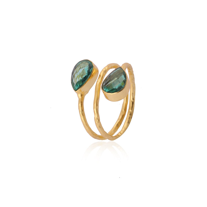 The Cleo Gold Ring by Watermelon Tropical features two teardrop-shaped green gemstones at each end. The bands are slightly textured, giving a hammered appearance to the piece. The faceted gemstones add a touch of elegance and sparkle.