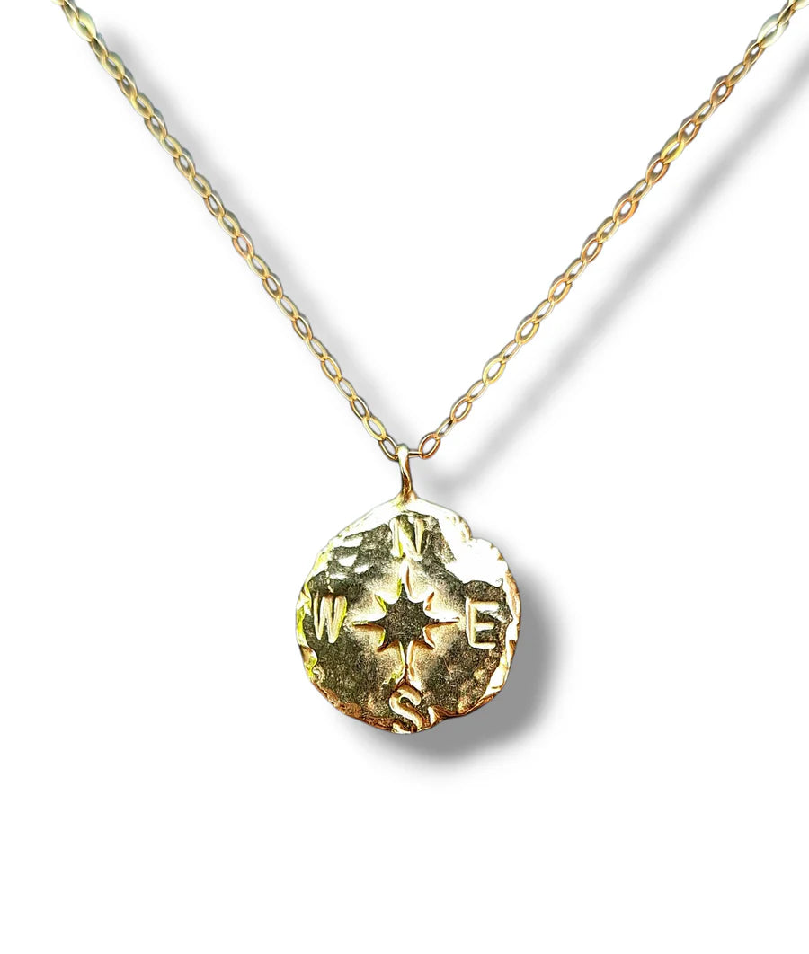 The Pale Raven Compass Coin Gold Plated Necklace features an oval link chain and a round, textured pendant engraved with N, E, S, and W—a timeless handcrafted piece perfect for everyday wear.