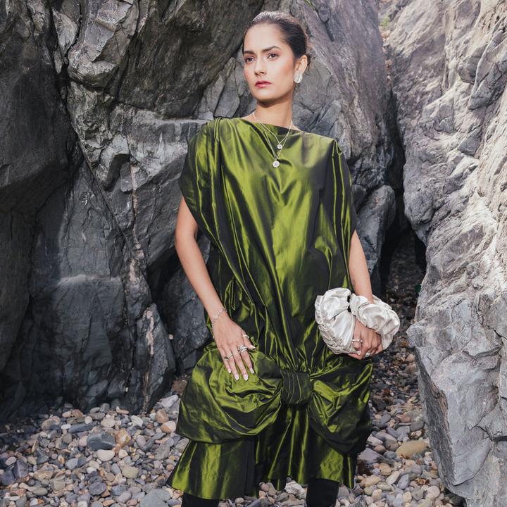 Model wearing Tide Studs Large, silver-toned textured disc earrings, with a green satin dress against coastal rocks.