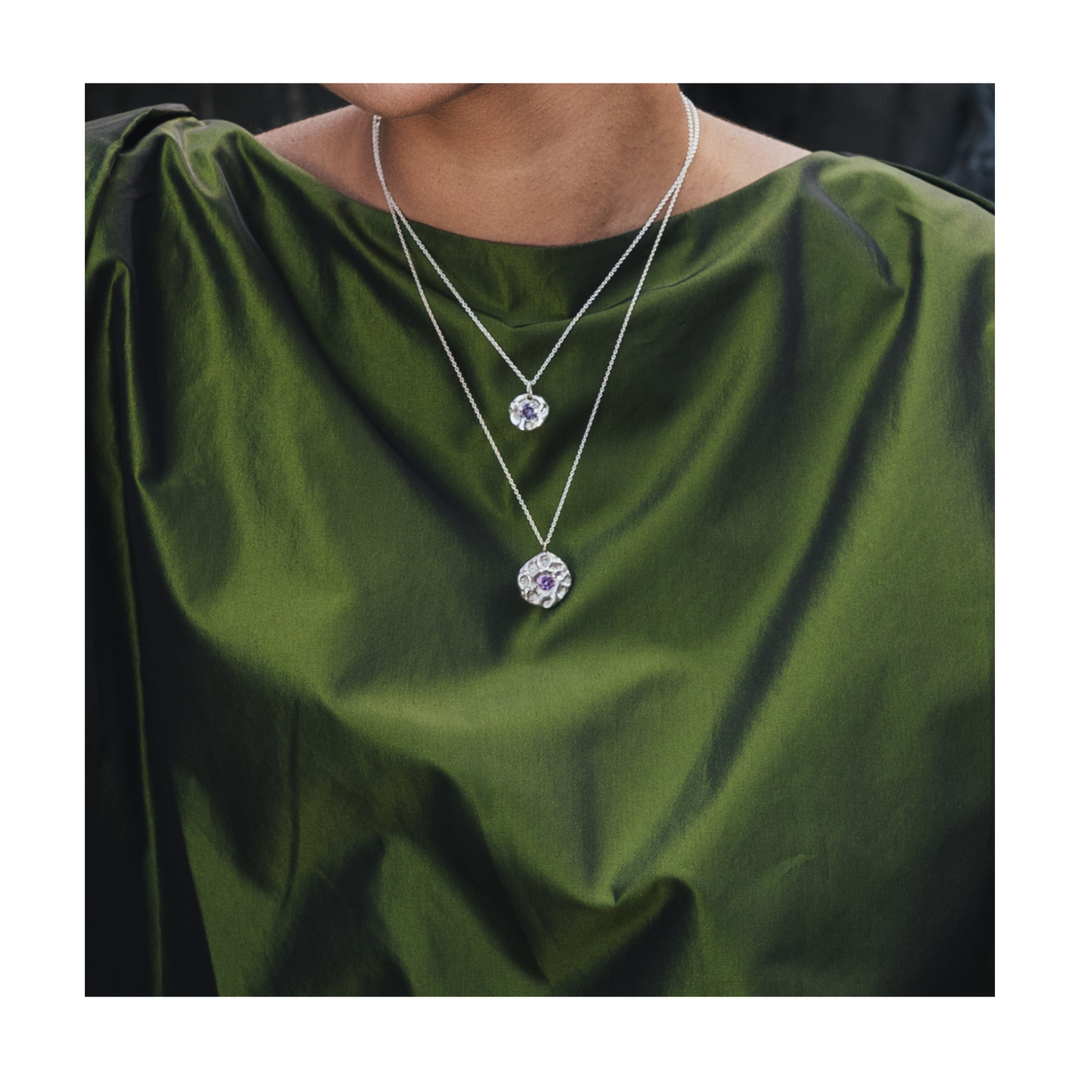 A close-up of a person wearing a double-layered silver necklace with round clear gemstone pendants, styled with an olive green top.