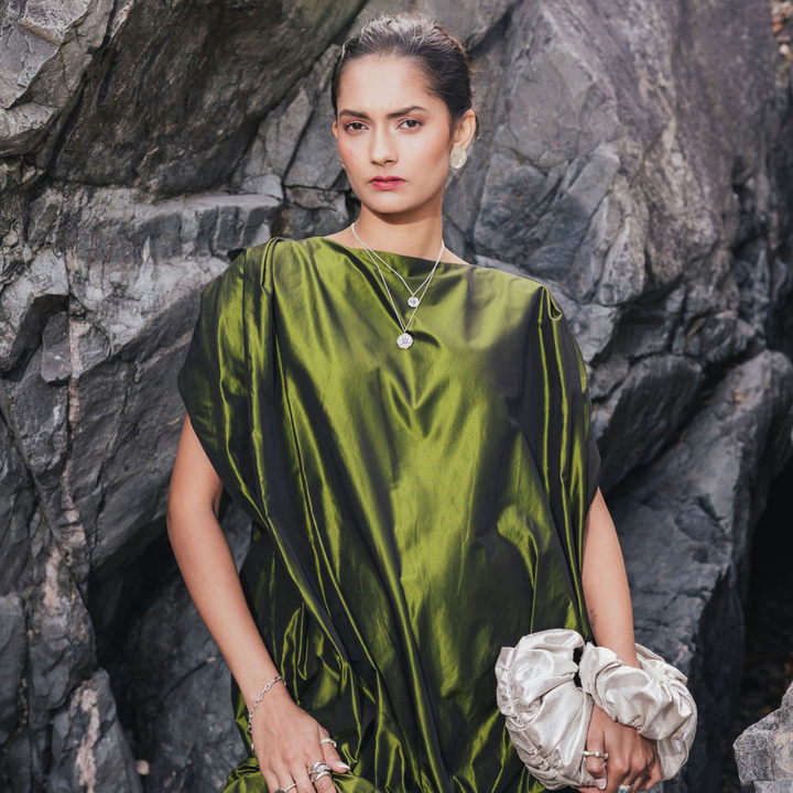Model wearing the Multi Stone Moissanite Silver Necklace layered with a smaller pendant over a green satin dress against coastal rocks.