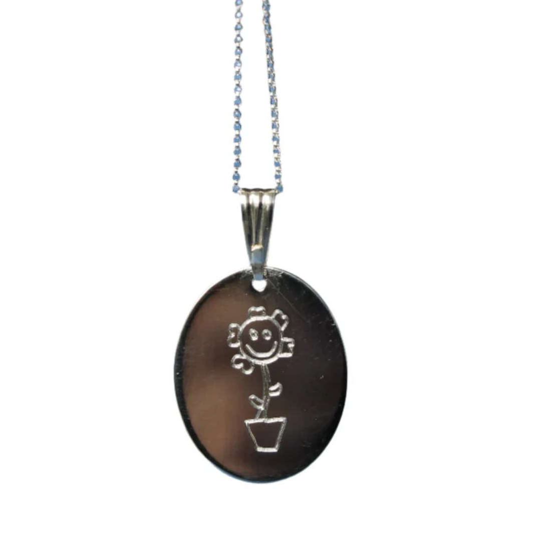 The Collective Dublin Personalised Kids Drawing Pendant is a silver oval necklace engraved with a smiling flower in a pot, inspired by children’s artwork, shown on a delicate chain against a plain white background.