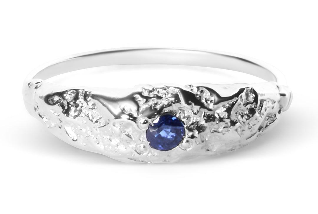 The Dublin Bay Silver Ring with Sapphire by Ava Jane Jewellery is a handmade sterling silver ring featuring an organic textured design and a single round blue sapphire at the center.