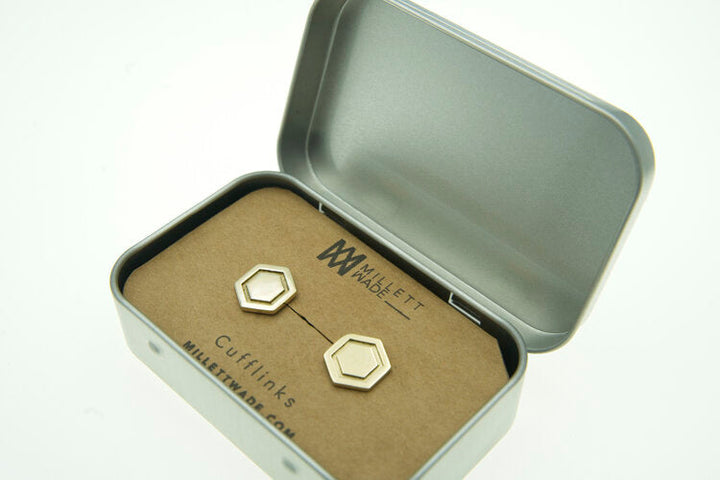 A metal box with a pair of Hexagon Cufflinks resting on a cardboard insert. The insert is branded with "Millett Wade." The box lid is partly open, showcasing the elegant and minimalist design of the hand-finished cufflinks.