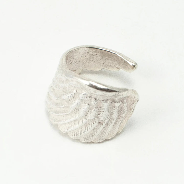 The Angel Wing Ring by Jennifer Kinnear is an open sterling silver ring with a textured feather-like design, shown on a white background. Available in silver or gold.