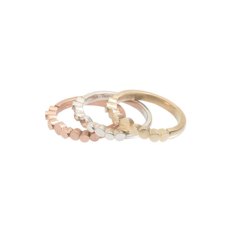 Three hexagon rings in different colors – rose gold, silver, and 9ct yellow gold – are pictured. Each Irish hallmarked ring features a series of small hexagonal shapes along the band. The made-to-order Flow Pebble Ring 9ct Yellow Gold by Miriam Wade is arranged in a neat, overlapping pattern.